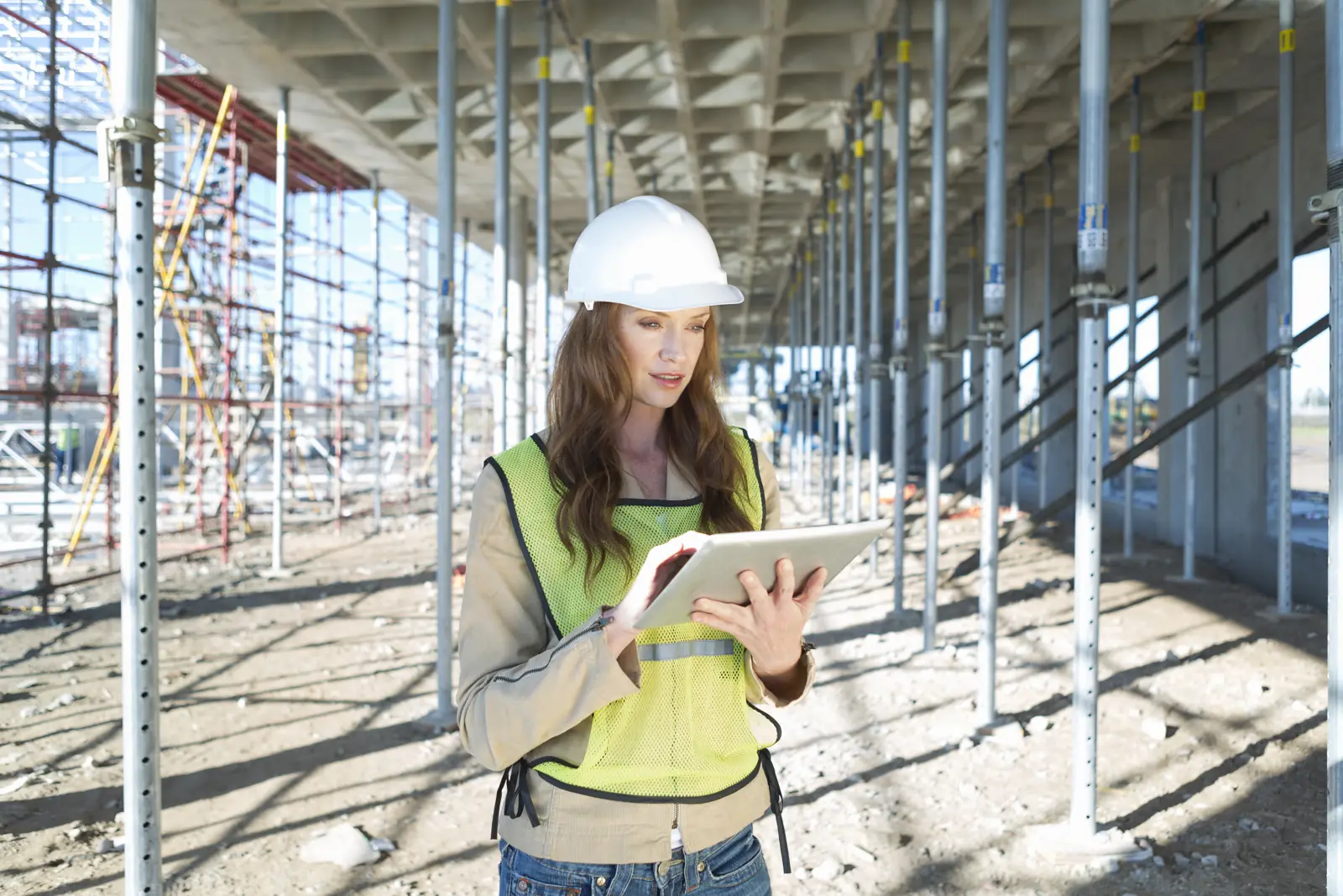 Site engineer in a hard hat reading a tablet among shoring posts